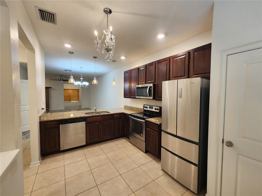 A kitchen features dark wood cabinets, stainless steel appliances, granite countertops, and tile flooring — 1112 HILLHURST DRIVE, WESLEY CHAPEL, FL