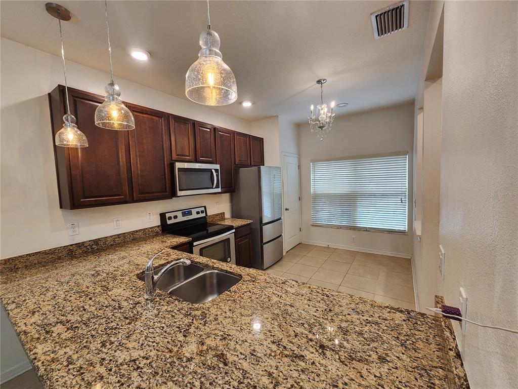 A kitchen features dark wood cabinets, granite countertops, stainless steel appliances, and pendant lighting — 1112 HILLHURST DRIVE, WESLEY CHAPEL, FL