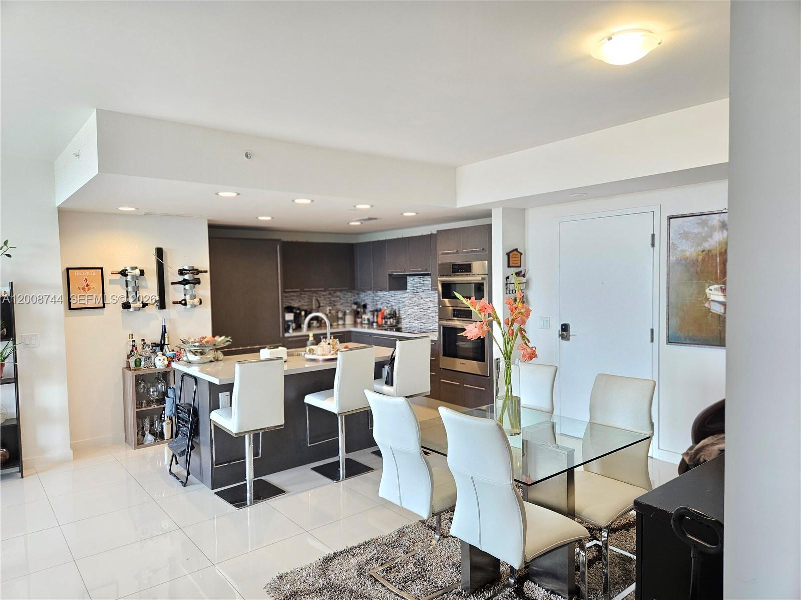 A modern kitchen with dark cabinetry, a central island, and an adjacent glass dining table — 7875 NW 107th Ave # 510, Doral FL 33178, DORAL, FL