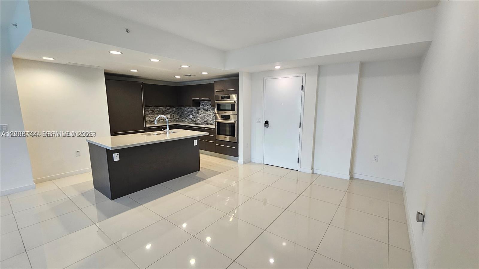 A modern kitchen features dark cabinetry, a central island, and light-colored tile flooring — 7875 NW 107th Ave # 510, Doral FL 33178, DORAL, FL