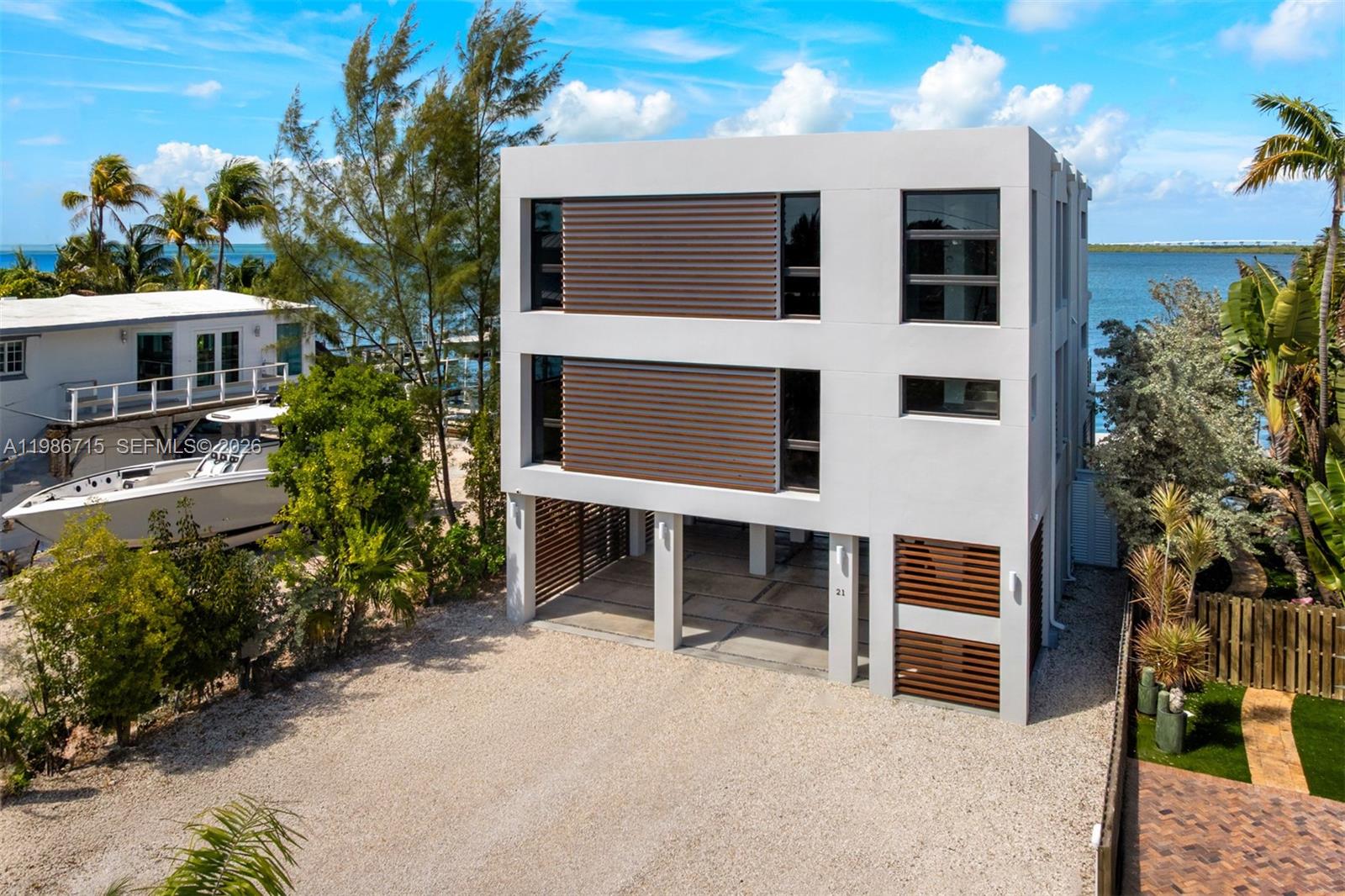 A modern, three-story white house with slatted wood accents stands on stilts near the water — 21 Stillwright Way, Key Largo FL 33037, KEY LARGO, FL