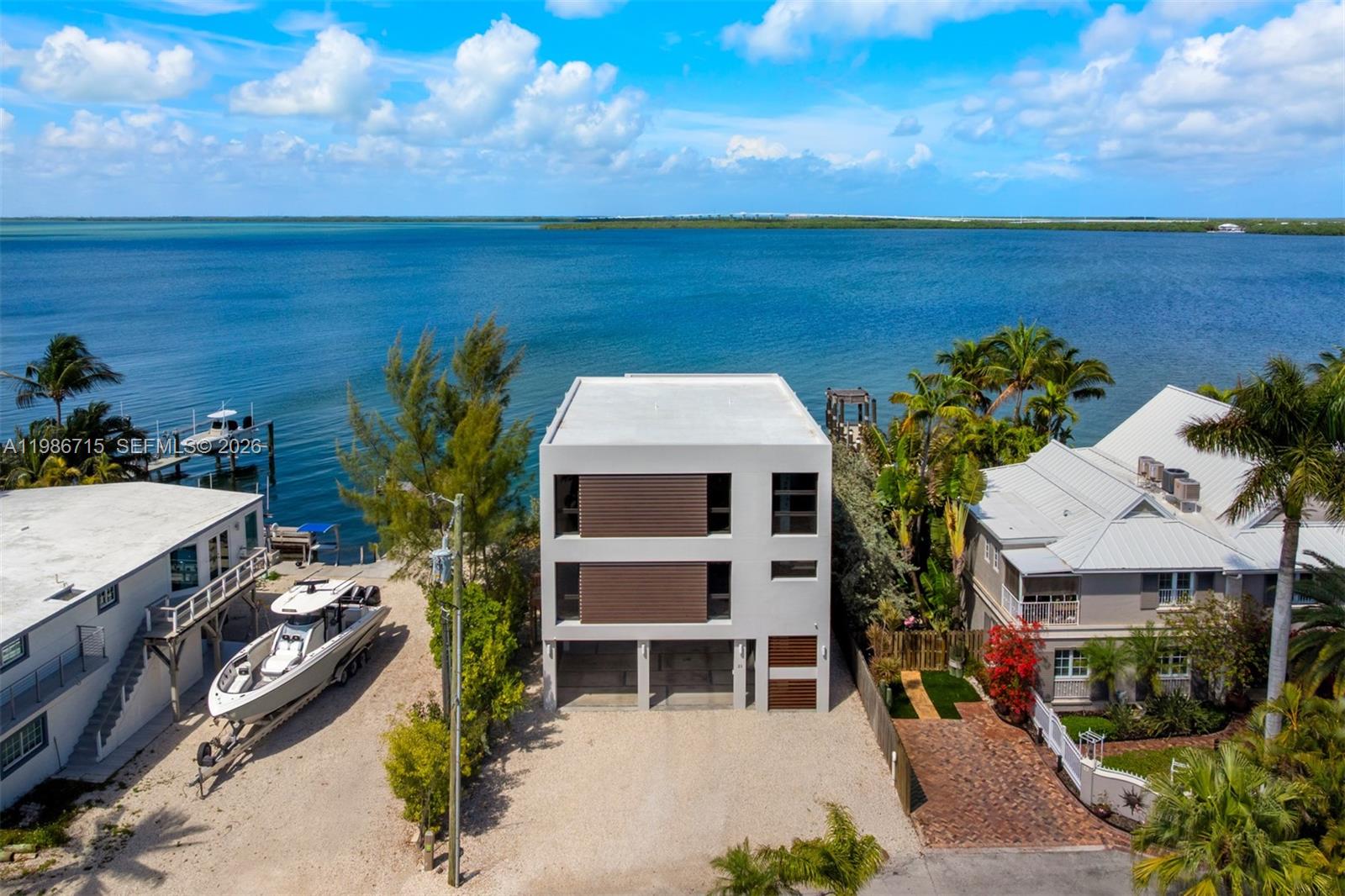 An aerial view shows a modern three-story house situated between a boat and a neighboring home — 21 Stillwright Way, Key Largo FL 33037, KEY LARGO, FL