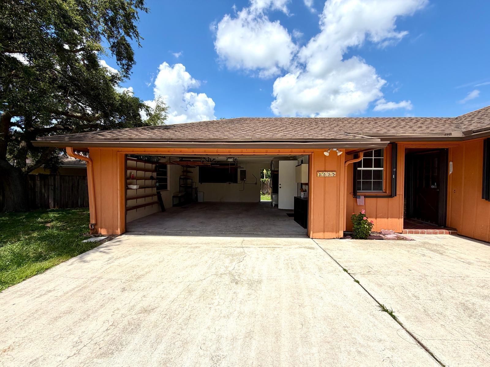 A view of a house exterior featuring an open garage, concrete driveway, and orange siding — 1235 Rowayton Circle, Wellington FL 33414, WELLINGTON, FL