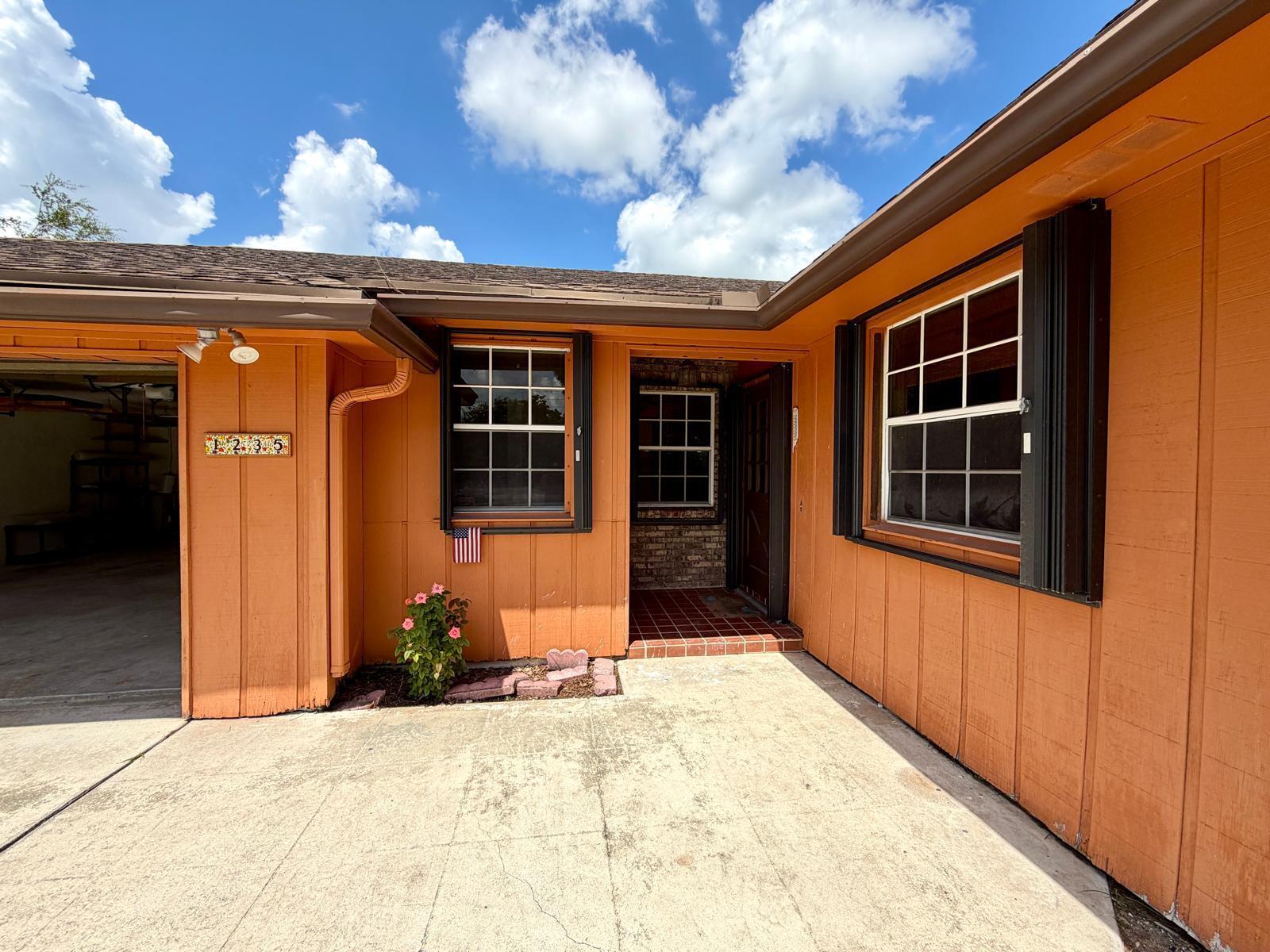 An exterior view of a house with orange siding, a concrete driveway, and a front entrance — 1235 Rowayton Circle, Wellington FL 33414, WELLINGTON, FL