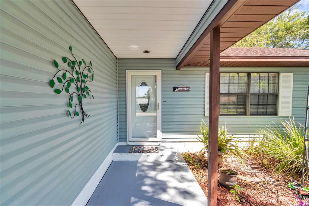 A covered front porch with light blue siding, a white front door, and metal wall art — 16365 SE 17TH STREET, OCKLAWAHA, FL