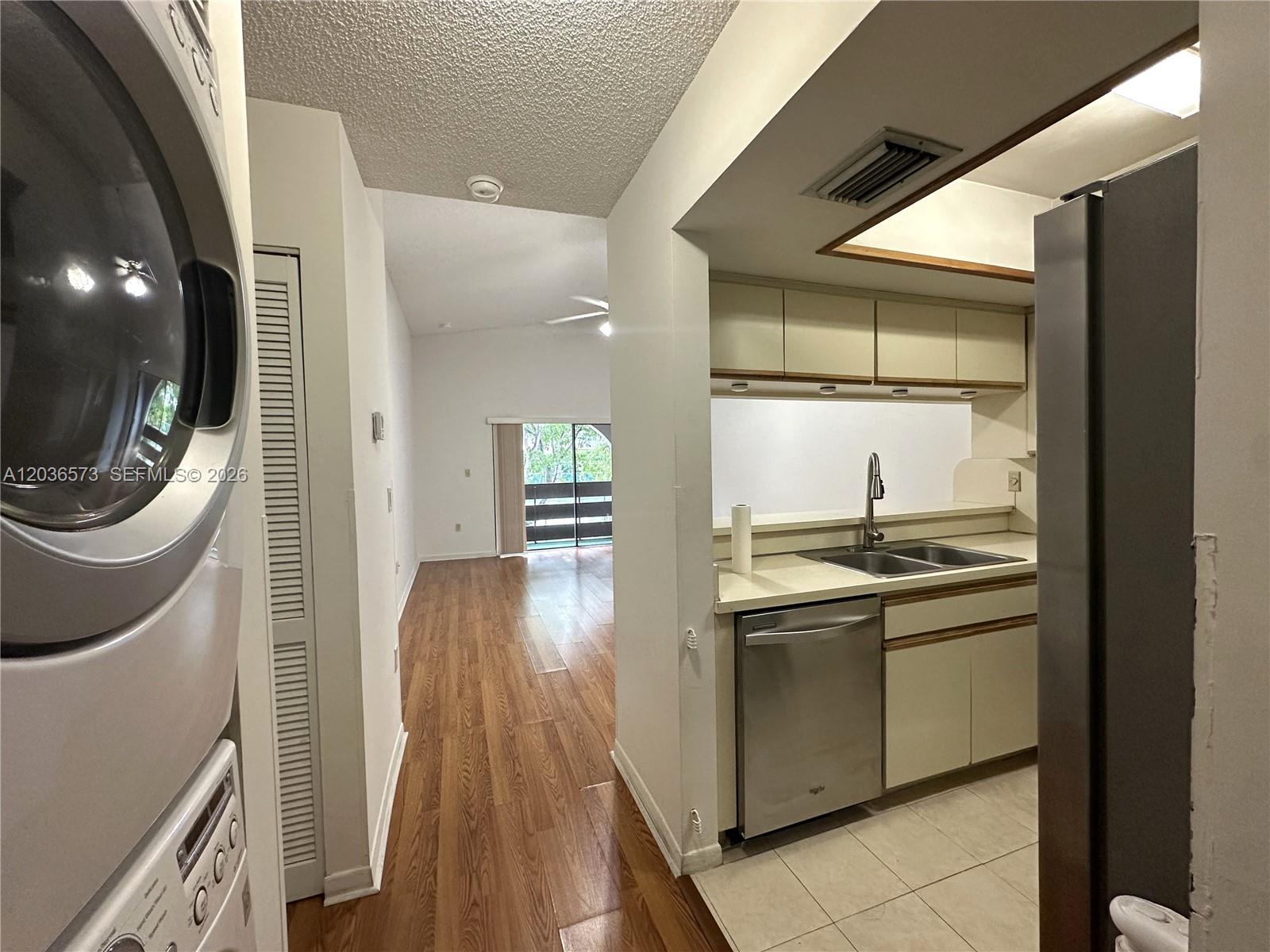 A kitchen with stainless steel appliances and tile flooring connects to a wood-floored living area — 8999 SW 123rd Ct # 212, Miami FL 33186, MIAMI, FL