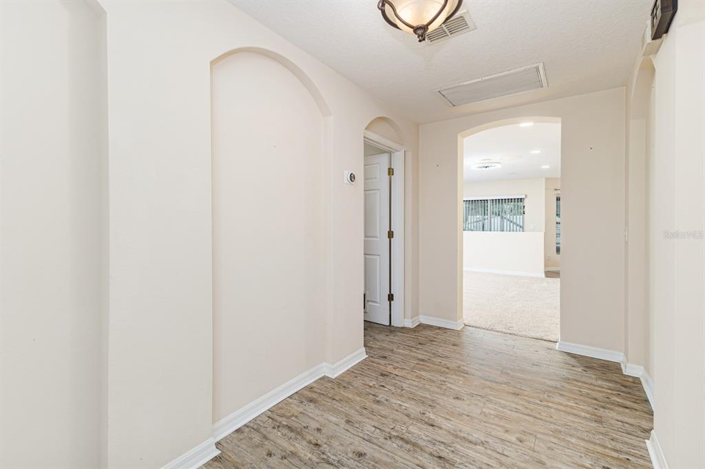 A hallway with wood-look flooring leads to an arched doorway opening into a carpeted room — 7233 WAKEVIEW DRIVE, DAVENPORT, FL