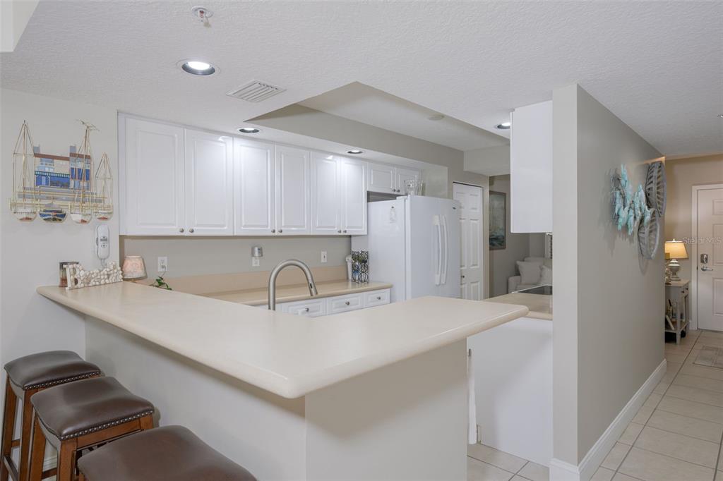 A kitchen features white cabinetry, a beige countertop breakfast bar, and three brown stools — 4650 LINKS VILLAGE DRIVE UNIT C206, PONCE INLET, FL