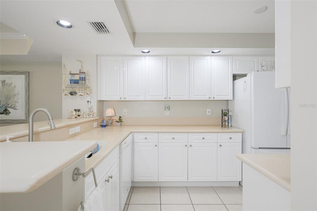 A kitchen features white cabinetry, light countertops, a white refrigerator, and tiled flooring — 4650 LINKS VILLAGE DRIVE UNIT C206, PONCE INLET, FL