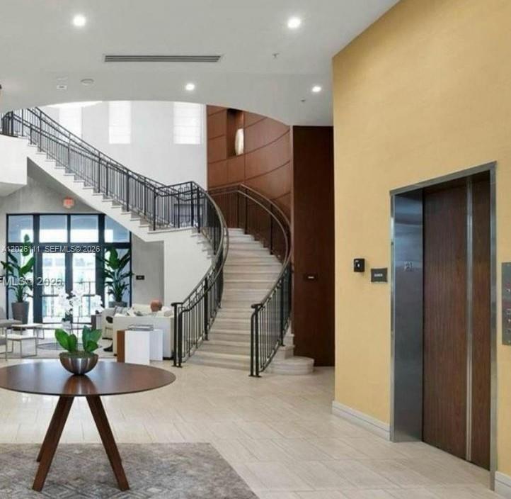 A grand foyer features a curved staircase, a round wooden table, and a modern elevator — 10620 NW 88th St # 221, Doral FL 33178, DORAL, FL