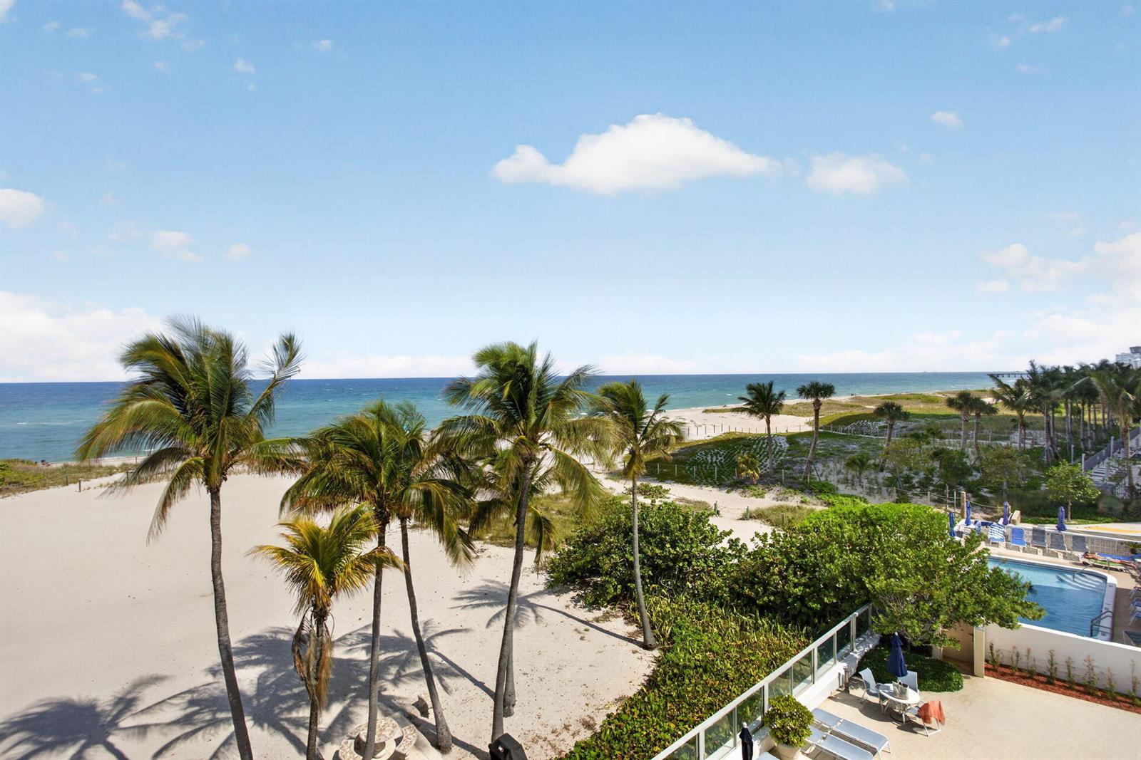 An elevated view of a sandy beach with palm trees and a swimming pool below — 1012 N Ocean Boulevard # 408, Pompano Beach FL 33062, POMPANO BEACH, FL