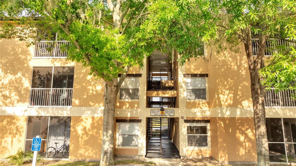 A three-story apartment building exterior features tan stucco walls, screened balconies, and a central staircase — 8825 LATREC AVENUE UNIT 6103, ORLANDO, FL