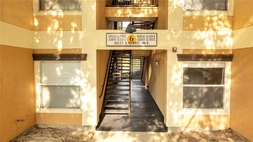 An exterior view of an apartment building entrance featuring a central staircase and unit signage — 8825 LATREC AVENUE UNIT 6103, ORLANDO, FL