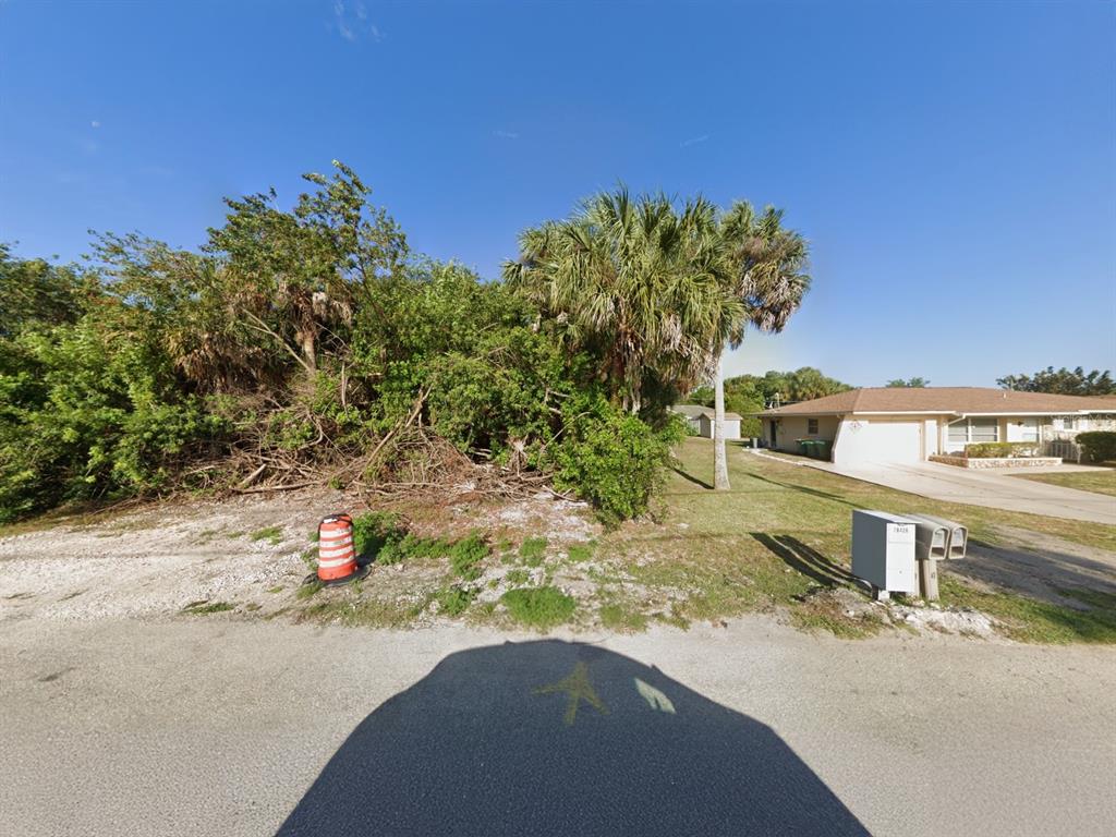 A vacant, overgrown lot sits next to a single-story house under a clear blue sky — 18425 DRIGGERS AVENUE, PORT CHARLOTTE, FL