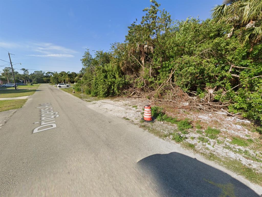 A paved street with a traffic cone sits beside a vacant, overgrown lot with trees — 18425 DRIGGERS AVENUE, PORT CHARLOTTE, FL