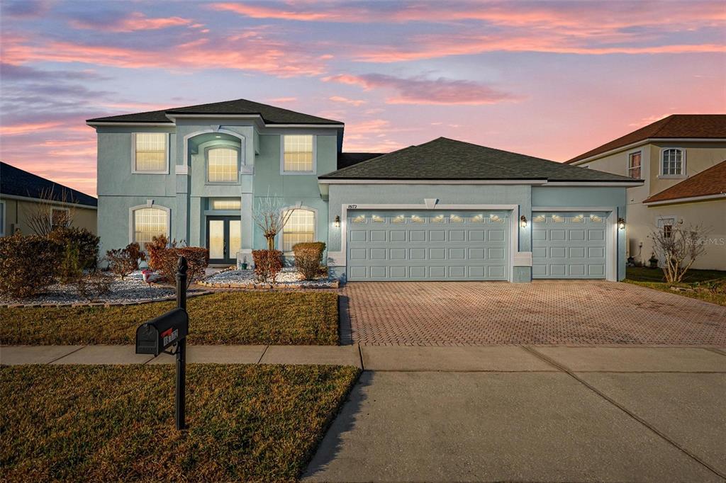 A two-story light blue house with a three-car garage and a paved driveway at sunset — 18172 THORNHILL GRAND CIRCLE, ORLANDO, FL