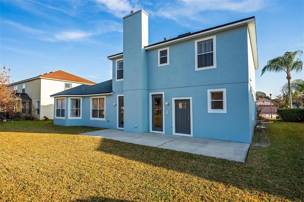 The exterior of a two-story light blue house features a concrete patio and a chimney — 18172 THORNHILL GRAND CIRCLE, ORLANDO, FL