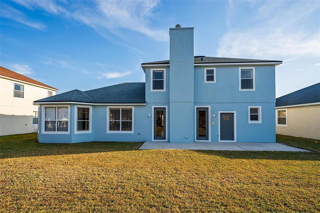 The rear exterior of a two-story light blue house features a chimney and concrete patio — 18172 THORNHILL GRAND CIRCLE, ORLANDO, FL