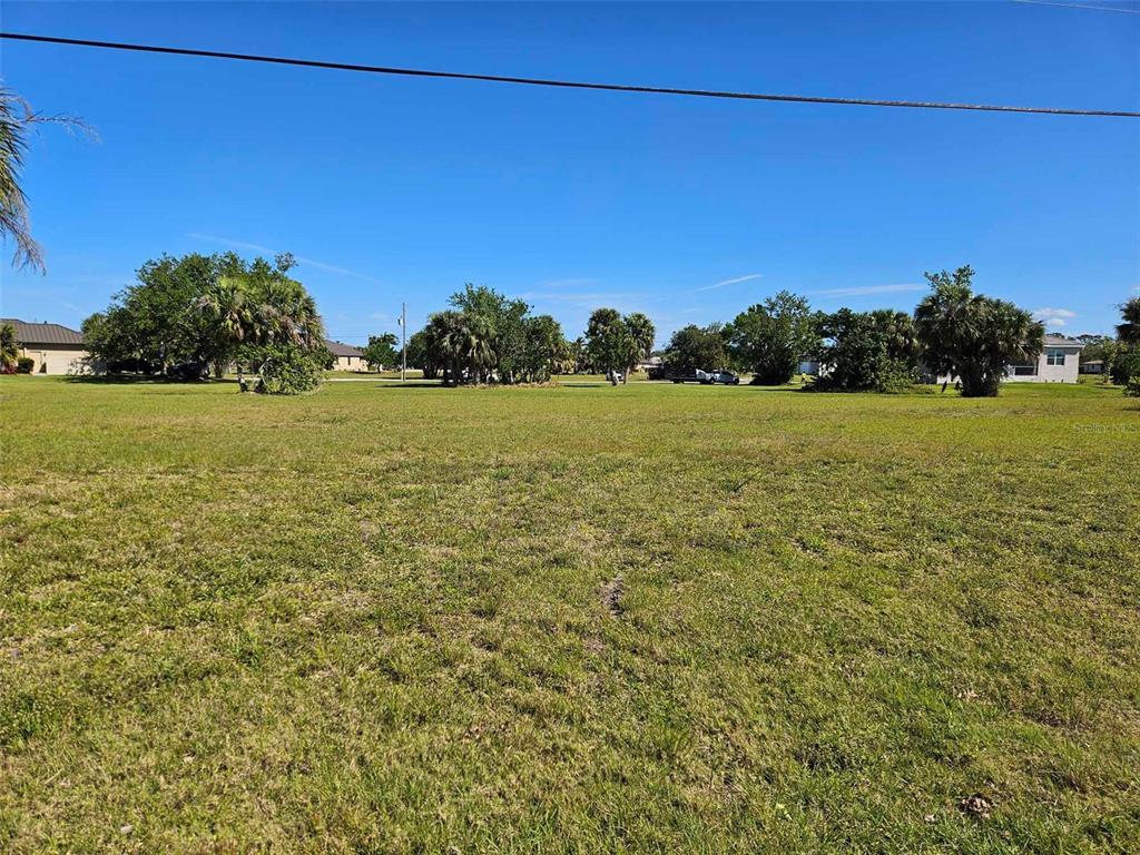 A large, flat, grassy vacant lot is surrounded by trees and residential houses — 24252 PEPPERCORN ROAD, PUNTA GORDA, FL