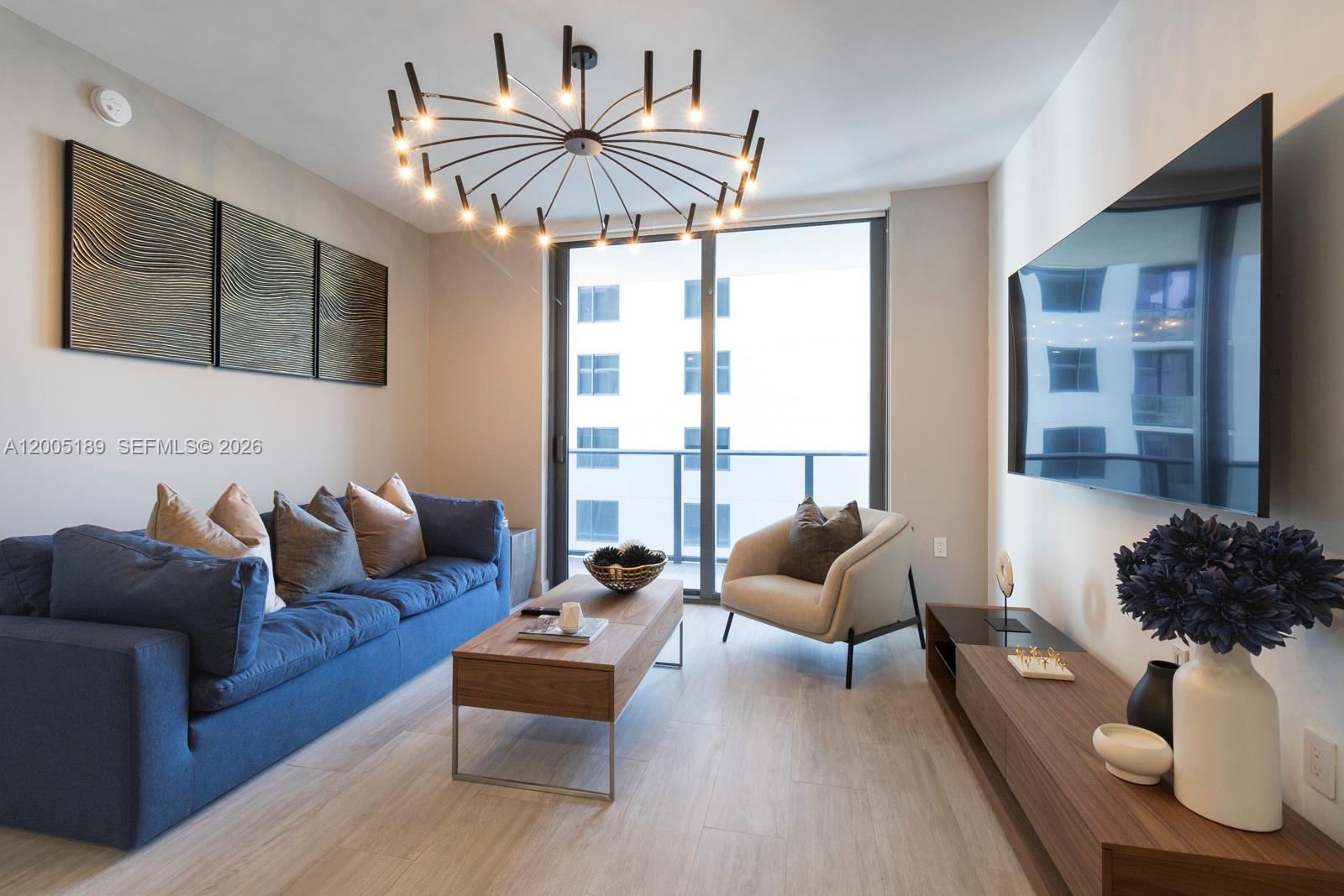 A living room features a blue sofa, wood coffee table, accent chair, and modern chandelier — 55 SW 9th St # 3010, Miami FL 33130, MIAMI, FL