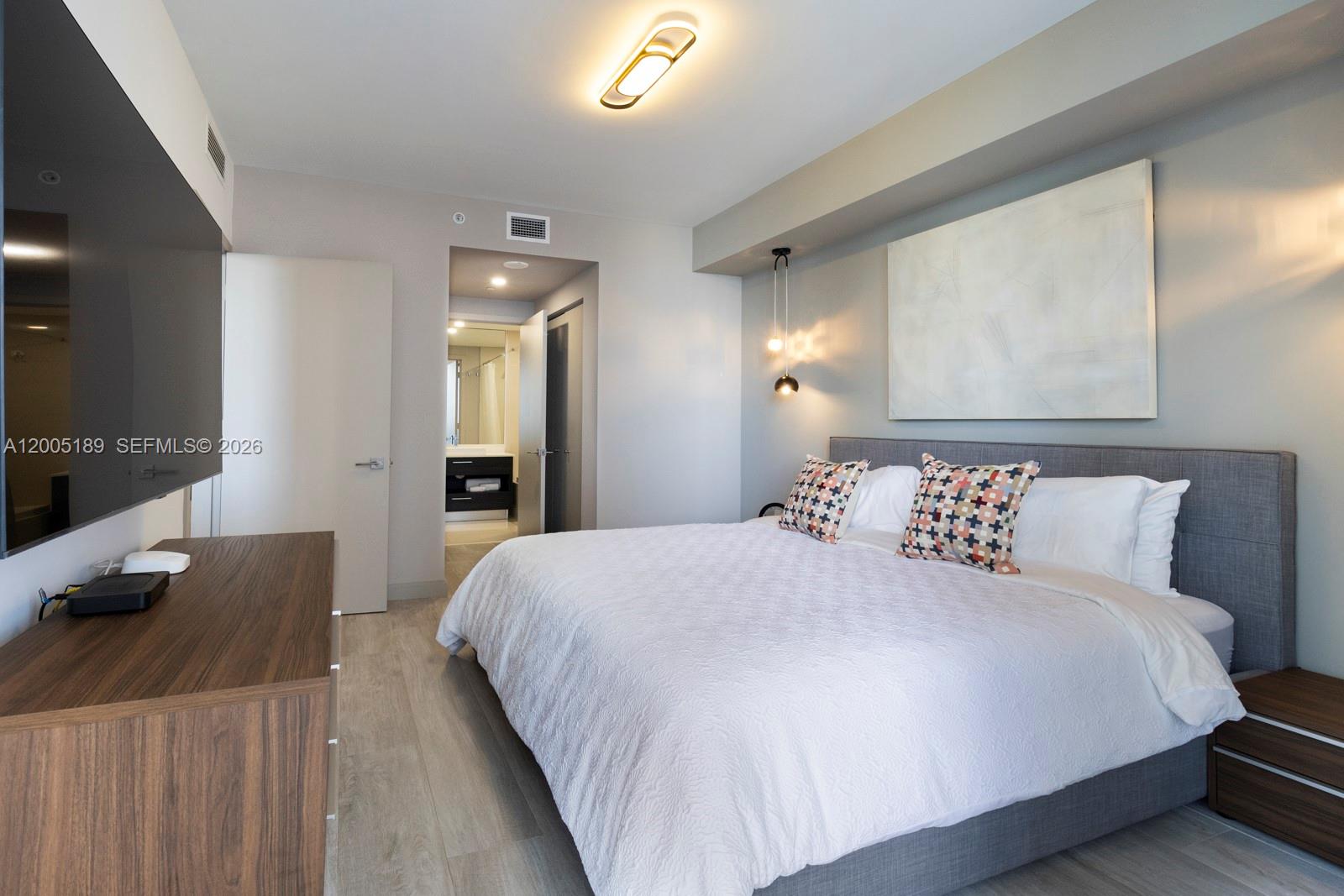 A bedroom features a bed with patterned pillows, a wall-mounted television, and an attached bathroom — 55 SW 9th St # 3010, Miami FL 33130, MIAMI, FL