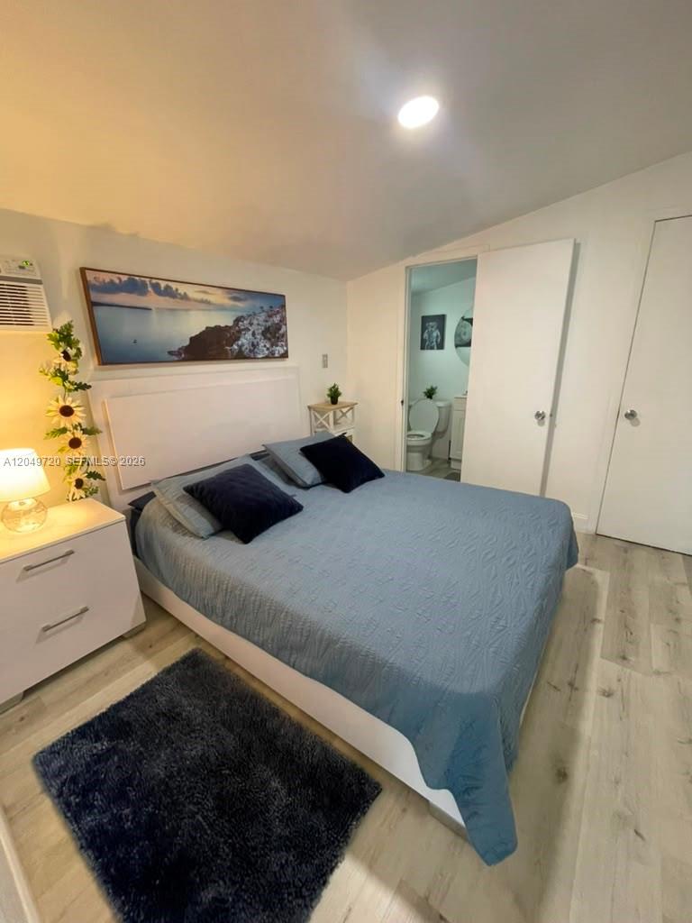 A bedroom features a bed with blue bedding, light wood flooring, and an attached bathroom — 5615 Hope St # 1, Hollywood FL 33021, HOLLYWOOD, FL