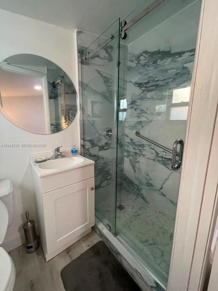 A bathroom features a white vanity, a round mirror, and a glass-enclosed marble-tiled shower — 5615 Hope St # 1, Hollywood FL 33021, HOLLYWOOD, FL
