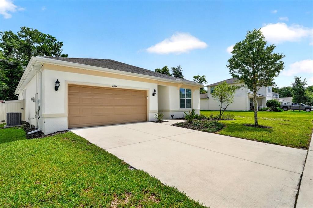 A single-story house with a beige stucco exterior, a two-car garage, and a concrete driveway — 2044 CANOPY TERRACE BOULEVARD, DELAND, FL