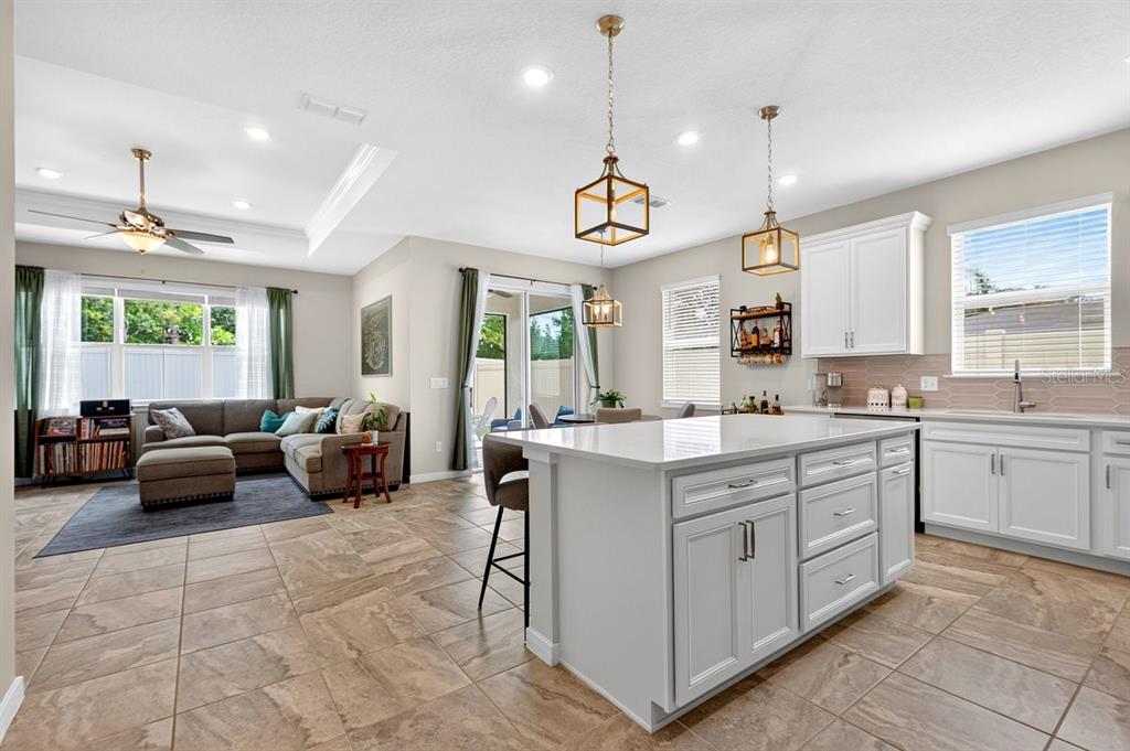 An open-concept kitchen and living area featuring a large island, tile floors, and pendant lighting — 2044 CANOPY TERRACE BOULEVARD, DELAND, FL