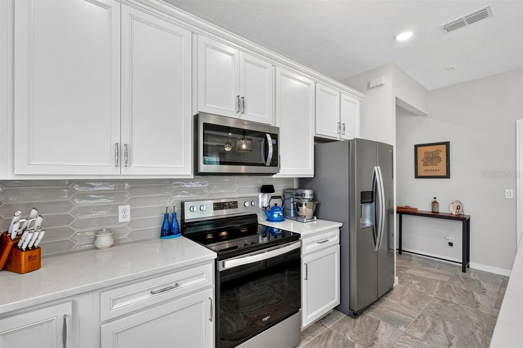A kitchen with white cabinets, stainless steel appliances, gray tile backsplash, and light countertops — 2044 CANOPY TERRACE BOULEVARD, DELAND, FL