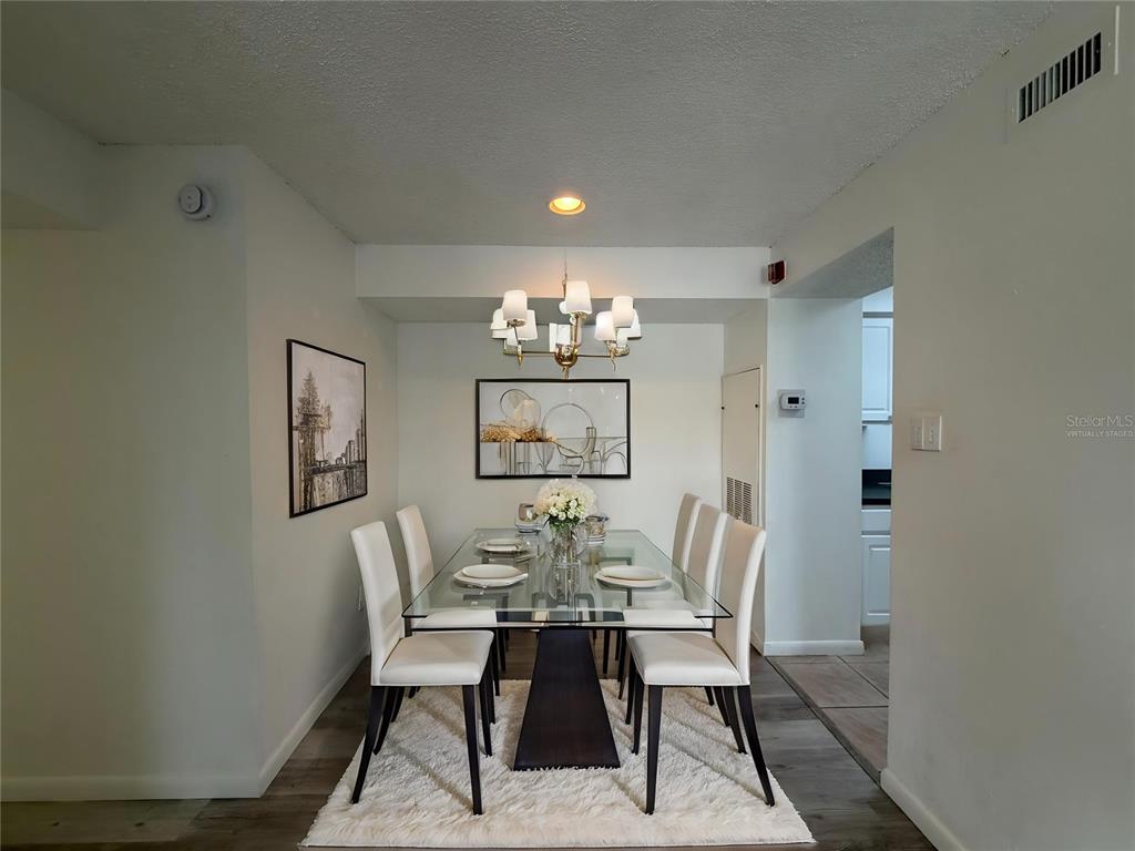 A dining room features a glass-topped table, six white chairs, and a chandelier on a rug — 3756 IDLEBROOK CIRCLE UNIT 108, CASSELBERRY, FL