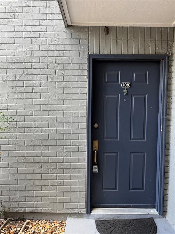 A dark blue front door with a lockbox is set into a gray brick wall — 3756 IDLEBROOK CIRCLE UNIT 108, CASSELBERRY, FL