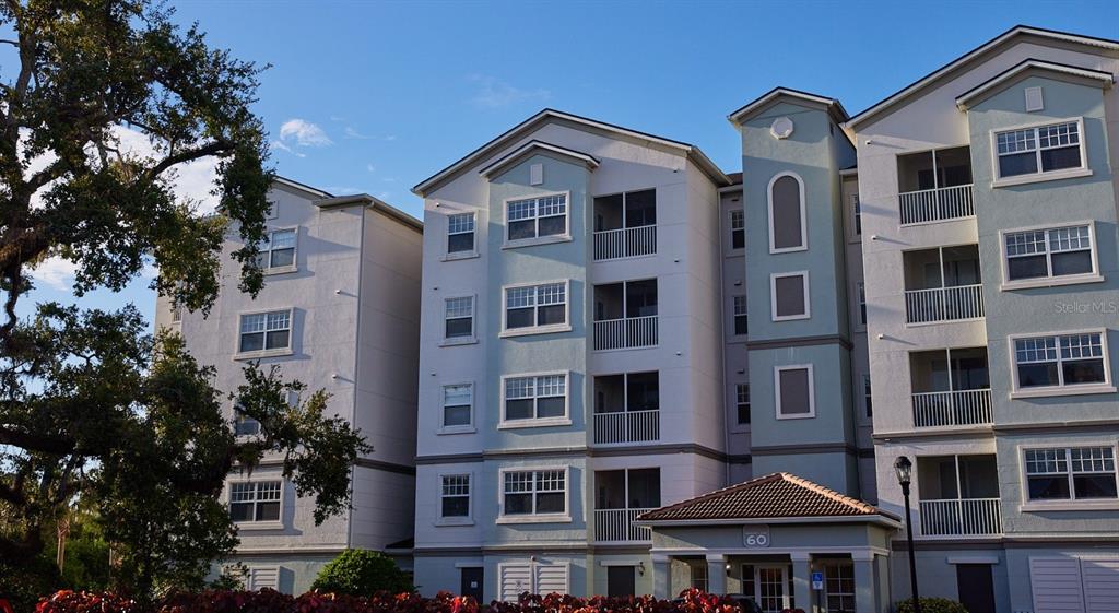 Exterior view of a multi-story apartment building with light-colored siding and screened balconies — 4 MAGGIE LANE UNIT Harmony, SARASOTA, FL