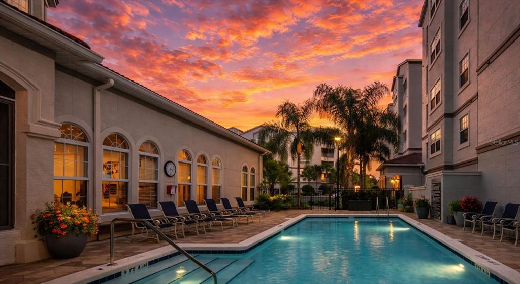 A swimming pool sits on a paved patio beside a multi-story building at sunset — 4 MAGGIE LANE UNIT Harmony, SARASOTA, FL