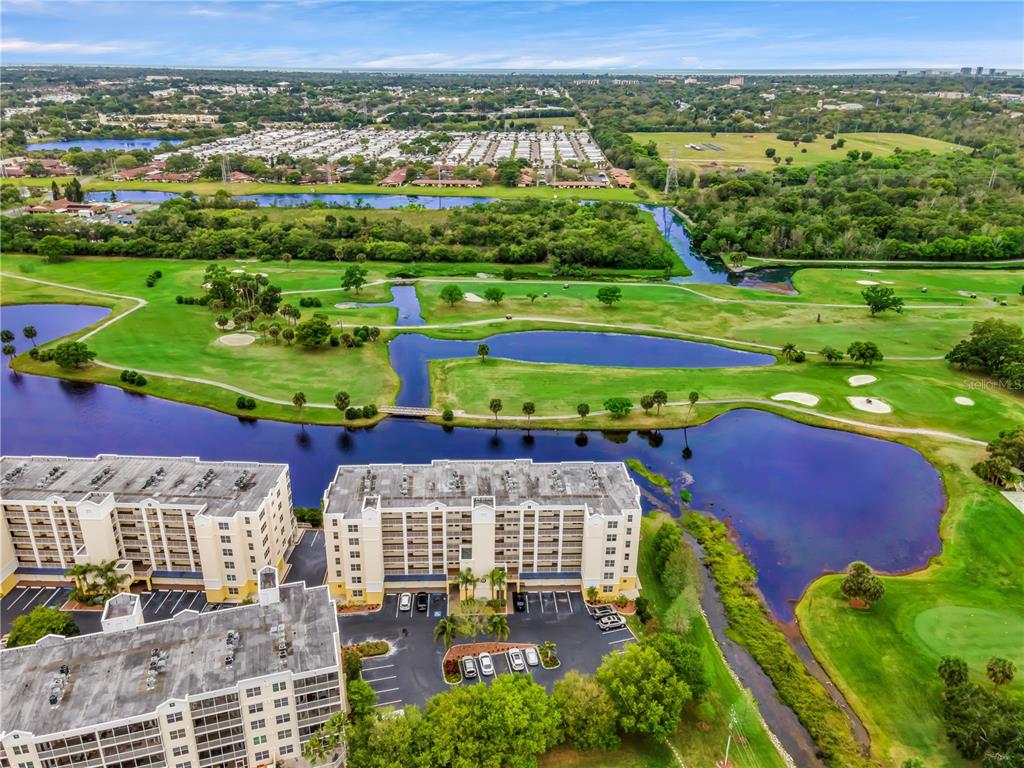 An aerial view shows multi-story apartment buildings situated next to a golf course and lake — 1200 COUNTRY CLUB DRIVE UNIT 5506, LARGO, FL