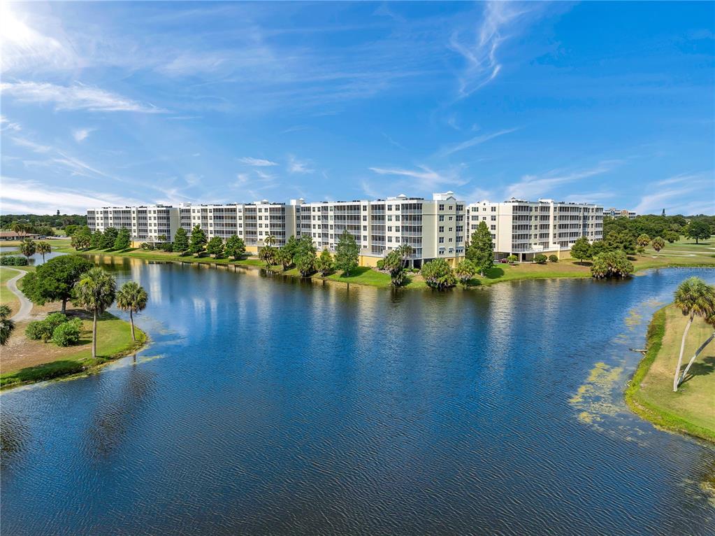 An aerial view of a large multi-story apartment building situated beside a lake — 1200 COUNTRY CLUB DRIVE UNIT 5506, LARGO, FL
