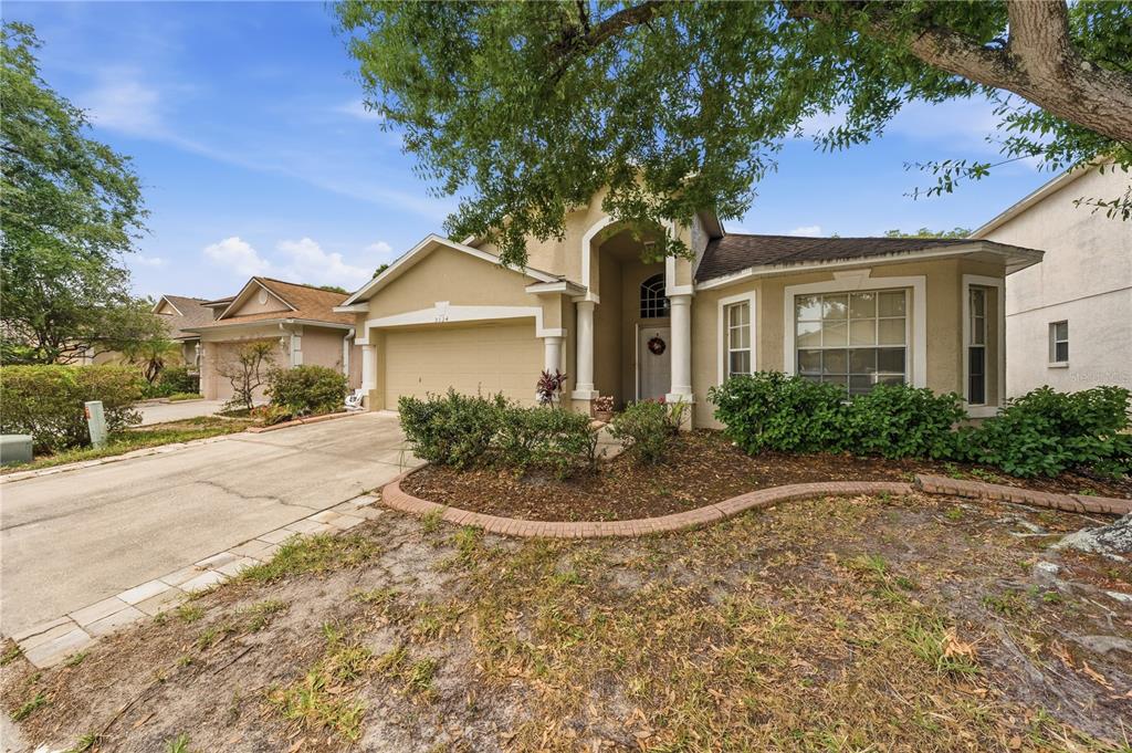 A single-story house with a beige stucco exterior, a two-car garage, and a front garden — 3324 MANOR COVE CIRCLE, RIVERVIEW, FL