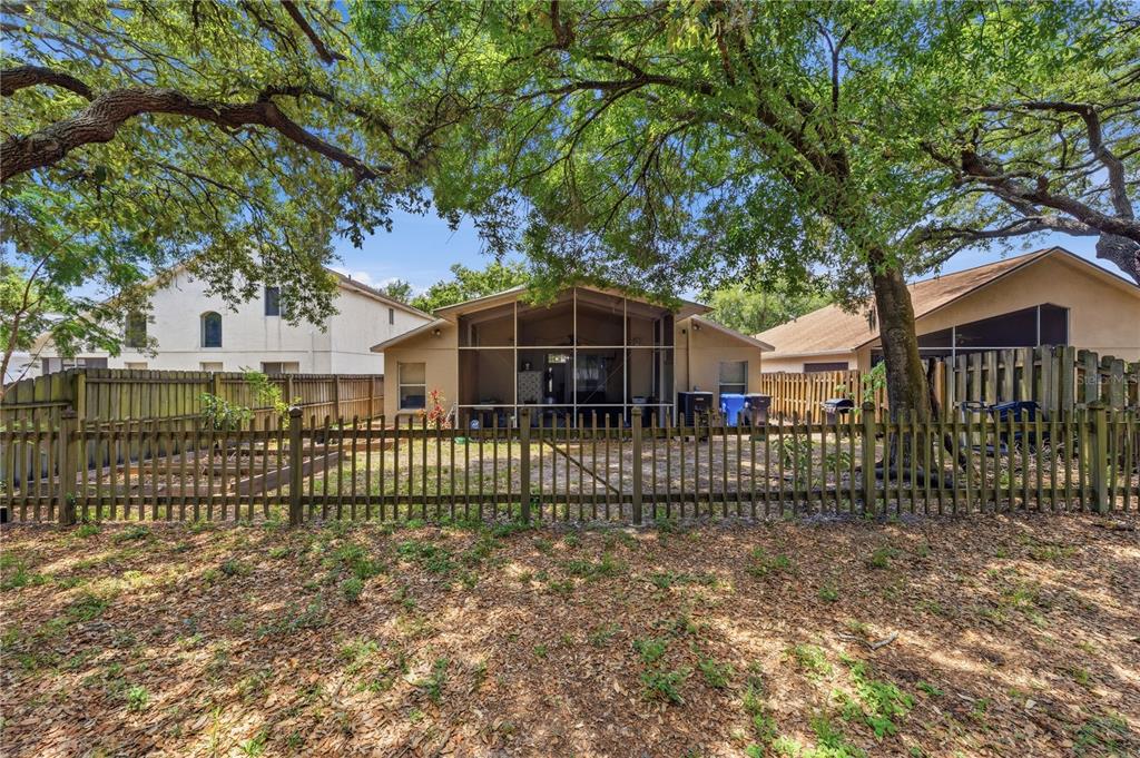 A fenced backyard features a screened-in patio attached to a single-story house under large trees — 3324 MANOR COVE CIRCLE, RIVERVIEW, FL