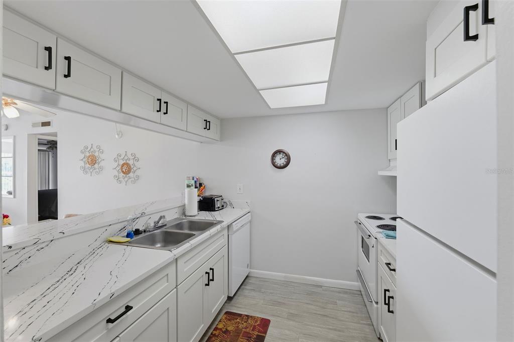 A galley kitchen features white cabinets, marble-patterned countertops, and a white appliance suite — 12760 INDIAN ROCKS ROAD UNIT 1082, LARGO, FL