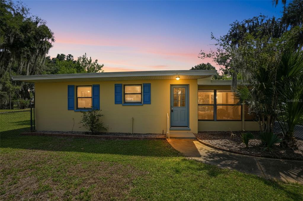 A yellow single-story house with blue shutters and a screened-in porch at dusk — 951 CR 453, LAKE PANASOFFKEE, FL