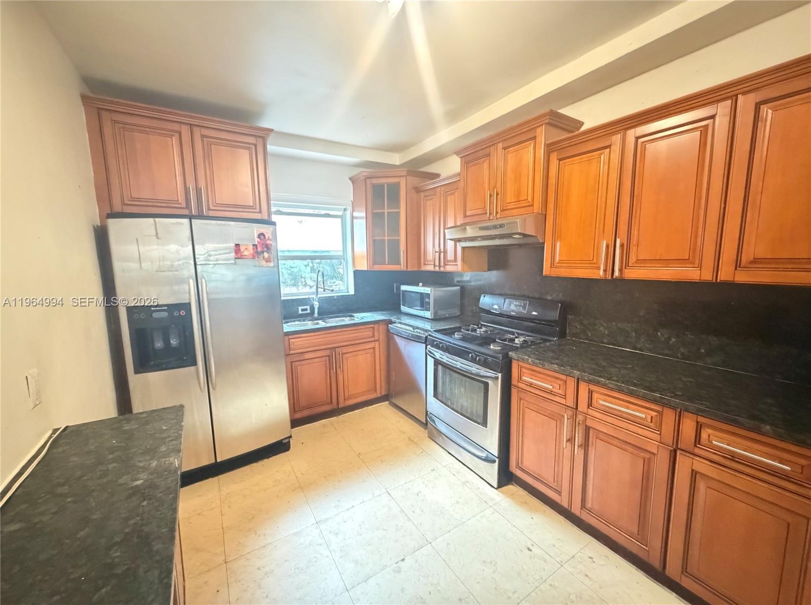 A kitchen features wooden cabinets, stainless steel appliances, and dark countertops over tiled floors — 2141 NE 124th St, North Miami FL 33181, NORTH MIAMI, FL
