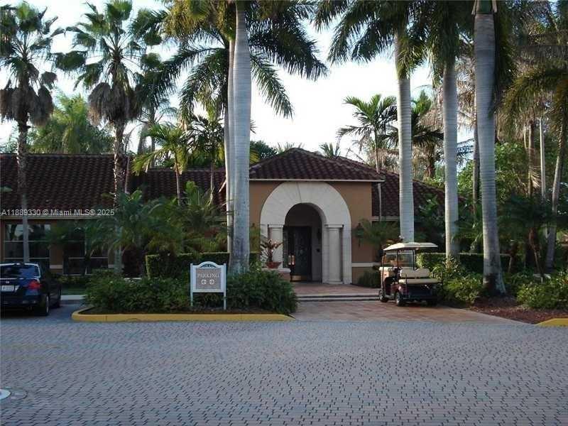 A paved driveway leads to a tan building entrance with an arched doorway and palm trees — 2173 Renaissance Blvd # 103, Miramar FL 33025, MIRAMAR, FL