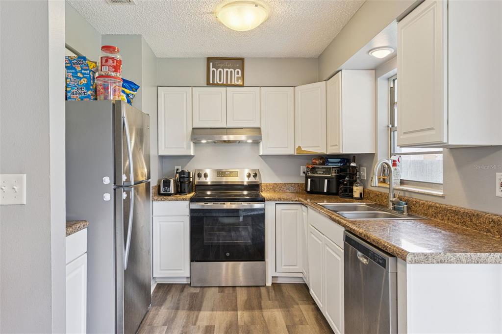 A kitchen features white cabinets, granite countertops, stainless steel appliances, and wood-look flooring — 2162 SWANSON DRIVE, DELTONA, FL