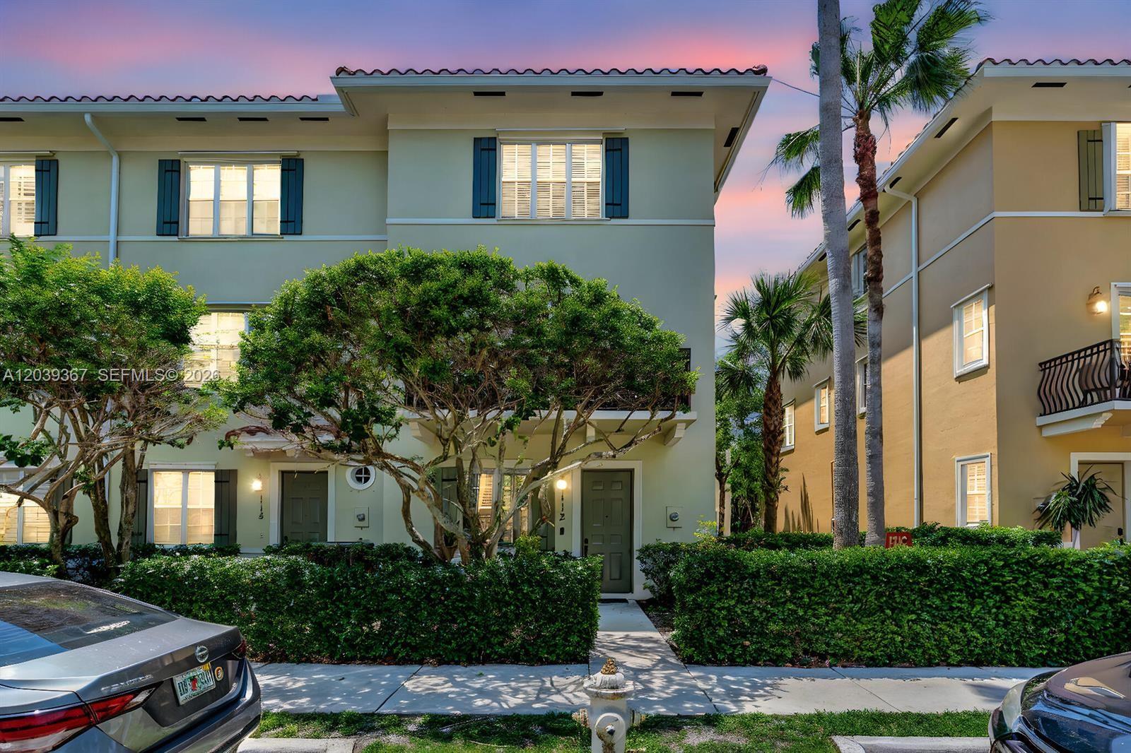 A three-story townhouse exterior features light green siding, dark shutters, and a landscaped front hedge — 112 Osceola Ln, Jupiter FL 33458, JUPITER, FL