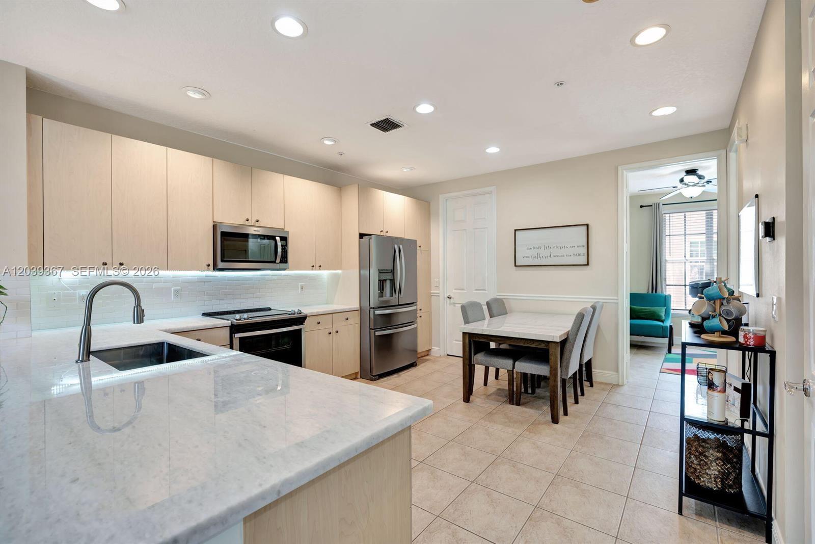 A kitchen with light wood cabinets, marble countertops, stainless steel appliances, and an adjacent dining area — 112 Osceola Ln, Jupiter FL 33458, JUPITER, FL