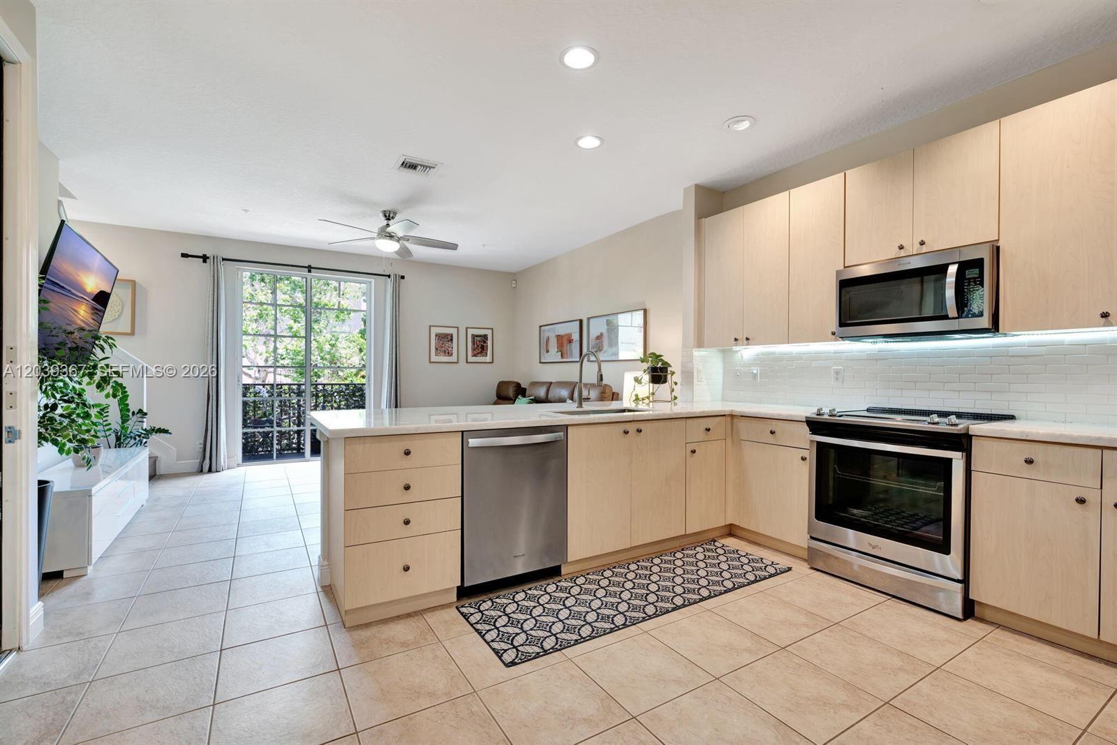 A kitchen with light wood cabinets, stainless steel appliances, and tile flooring opens to a living area — 112 Osceola Ln, Jupiter FL 33458, JUPITER, FL