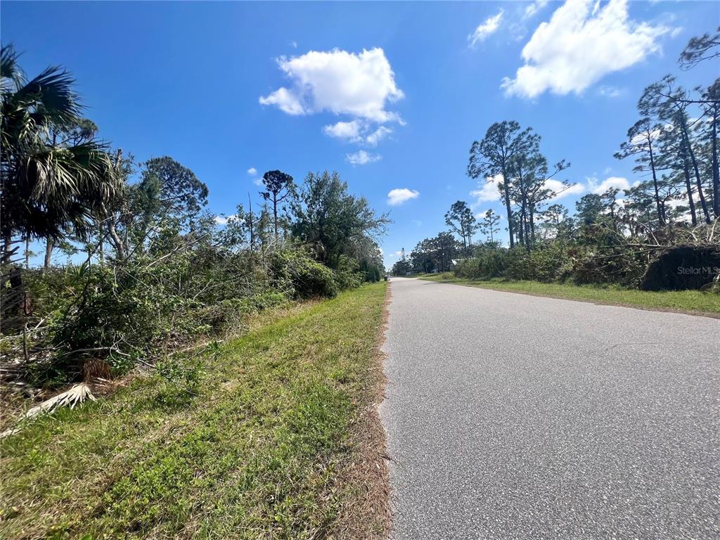 A paved road runs through a wooded area under a blue sky with clouds — 5252 ANDERSON ROAD, PORT CHARLOTTE, FL