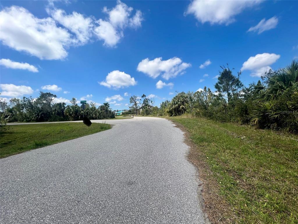 A paved road curves through a vacant, grassy lot with scattered trees under a blue sky — 5252 ANDERSON ROAD, PORT CHARLOTTE, FL