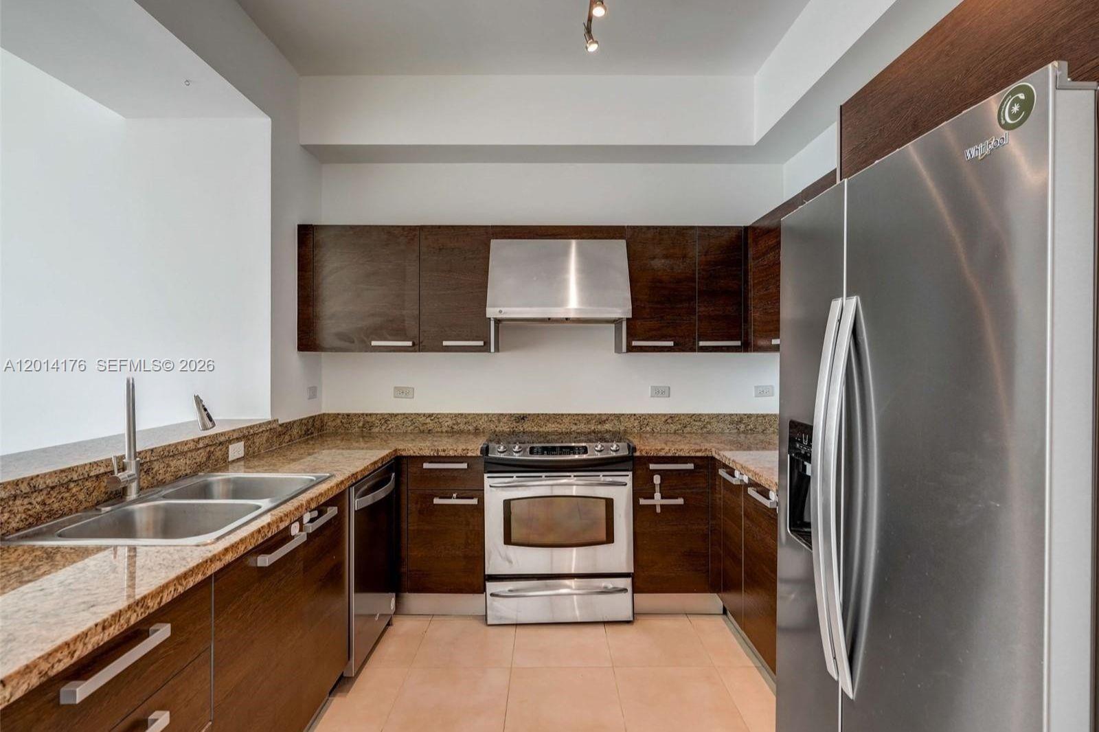 A kitchen features dark wood cabinets, granite countertops, and stainless steel appliances — MIAMI, FL