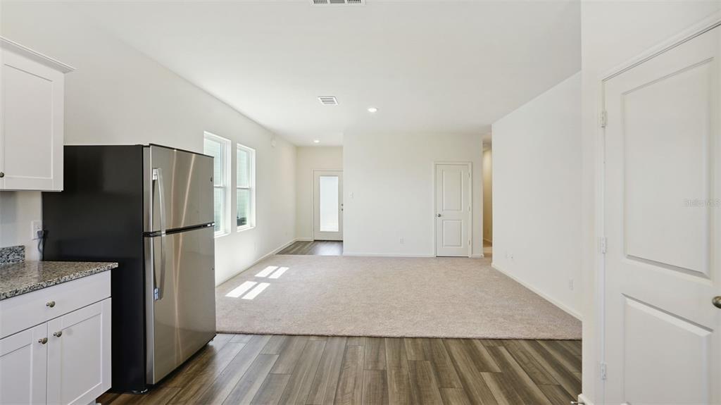A kitchen with stainless steel appliances opens into a carpeted living area with wood-look flooring — 5859 KALAMATA DRIVE, POLK CITY, FL